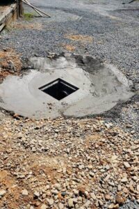 A heavy-duty catch basin installation with a green grate and smooth concrete collar set in a gravel parking lot, completed by a professional lawn care and storm water management service in Charlotte, NC."