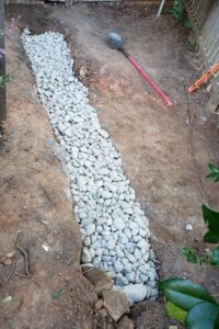 Top garden landscaping in Charlotte, NC, showcasing a residential yard drainage solution with a gravel trench designed to prevent standing water and improve soil health.