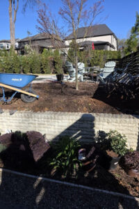 Top Gardens landscaping project in Charlotte, NC with fresh mulch beds, a block retaining wall, potted perennials, and a patio seating area