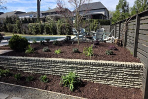 A backyard landscape installation by Top Gardens featuring a stone retaining wall, new potted plants, and fresh mulch beds in Charlotte, NC