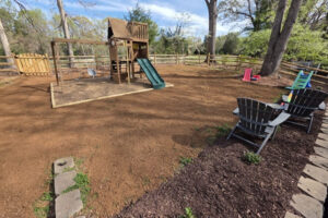 Large backyard playground area with fresh dark mulch, patio chairs, a wooden fence, and freshly graded topsoil prepped for lawn seeding in Charlotte, NC