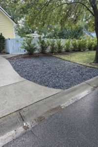 Professional top garden landscaping in Charlotte, NC, showcasing a newly installed black river rock feature along a residential driveway.