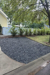 A completed top garden landscaping project featuring a clean dark gravel bed next to a driveway and fence line in Charlotte, NC.