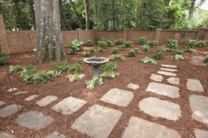 Professional mulching service in a Charlotte backyard garden with stepping stones and brick wall