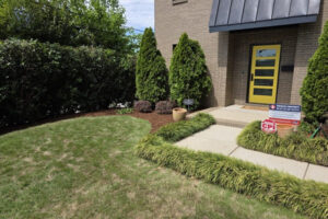 Top garden landscaping project in Charlotte, NC, showcasing a tidy front lawn, structured walkway borders, and manicured evergreen trees leading to a modern brick home entrance.